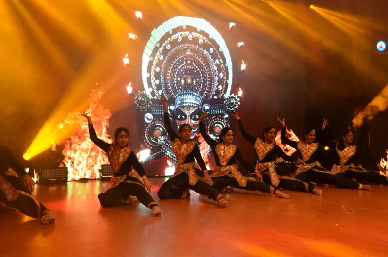 Children in colourful costumes dancing on a lit stage