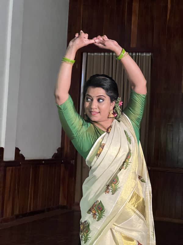 A dancer in a cream Kerala saree in a Mohiniyattam pose